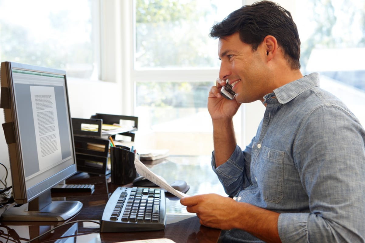 Businessman talking on the phone while looking at digital document on computer