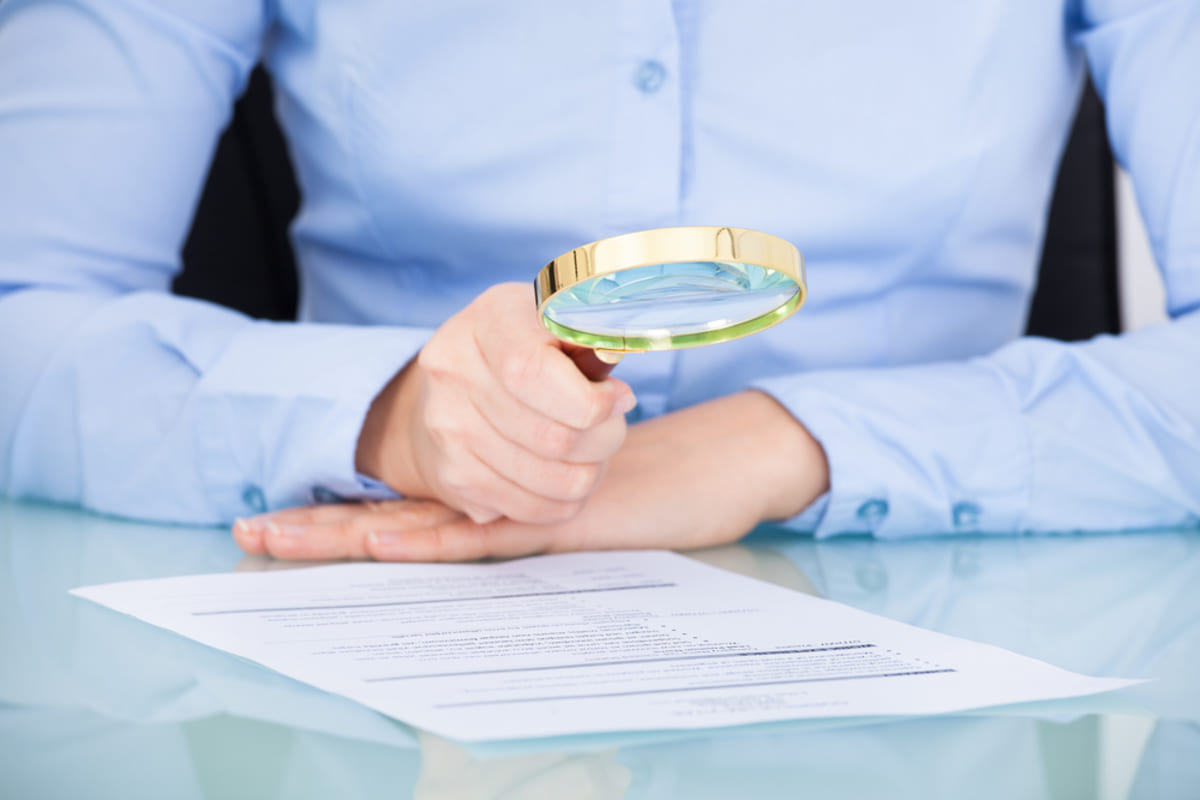 Businesswoman looking at document through magnifying glass.